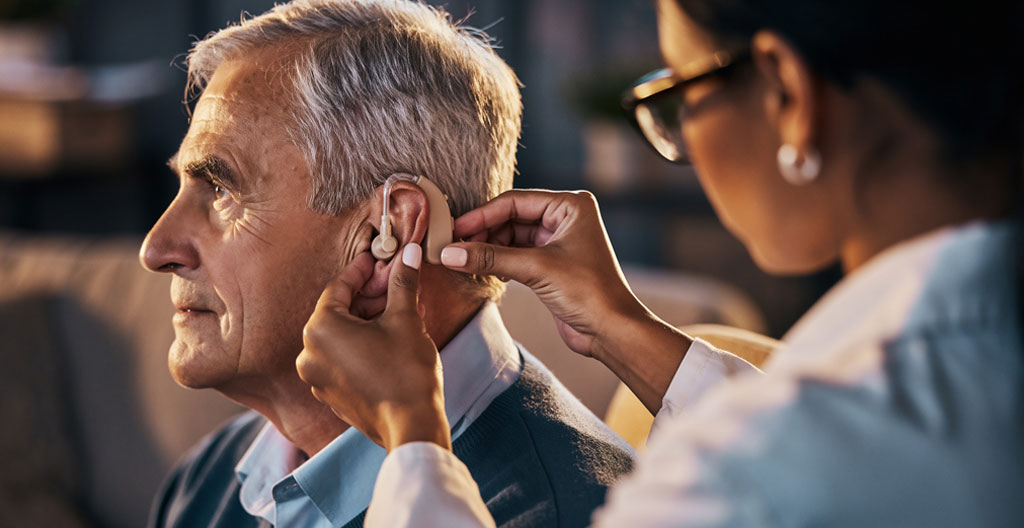 Senior de profil lors du réglage d'une aide auditive par un audioprothésiste